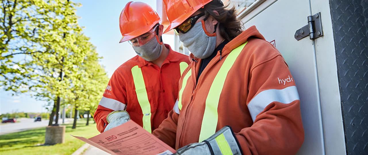 two Hydro One male employees working onsite in the snow reviewing paperwork